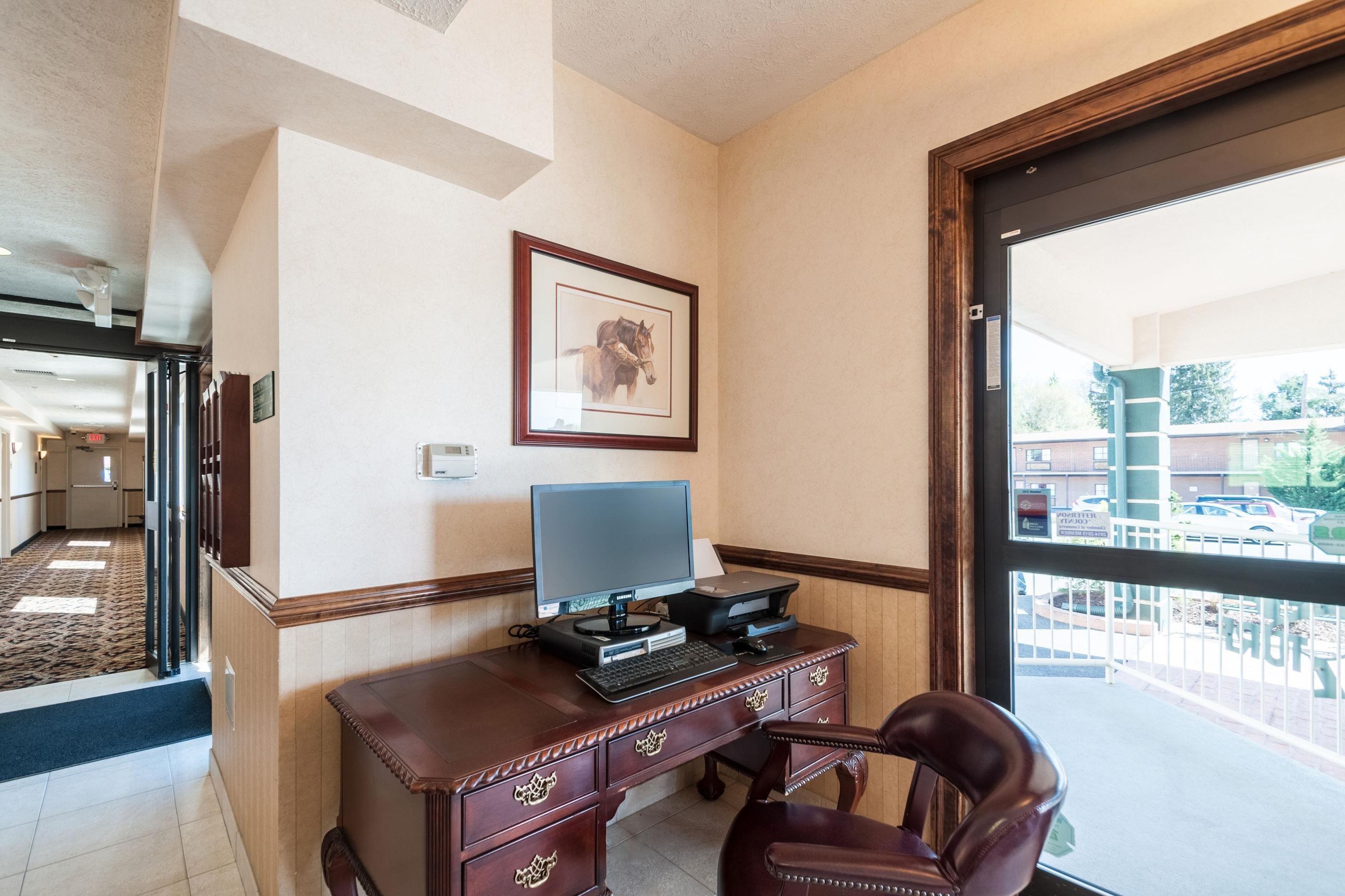 Habitación de hotel con escritorio, computadora, silla, un cuadro en la pared y vista al exterior a través de un ventanal grande.