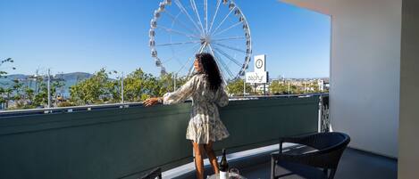 A balcony with a view of a Ferris wheel, a bottle of wine, and wicker furniture.