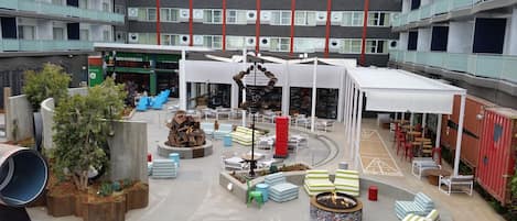 Un amplio atrio interior con varias zonas de estar, una chimenea central y una variedad de mobiliario de exterior.