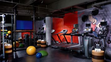 Un gimnasio con cintas de correr, pelotas de ejercicio y una pantalla de televisión.