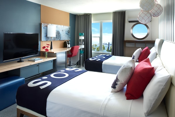 A hotel room with a bed, a desk, a TV, and a view of the city.