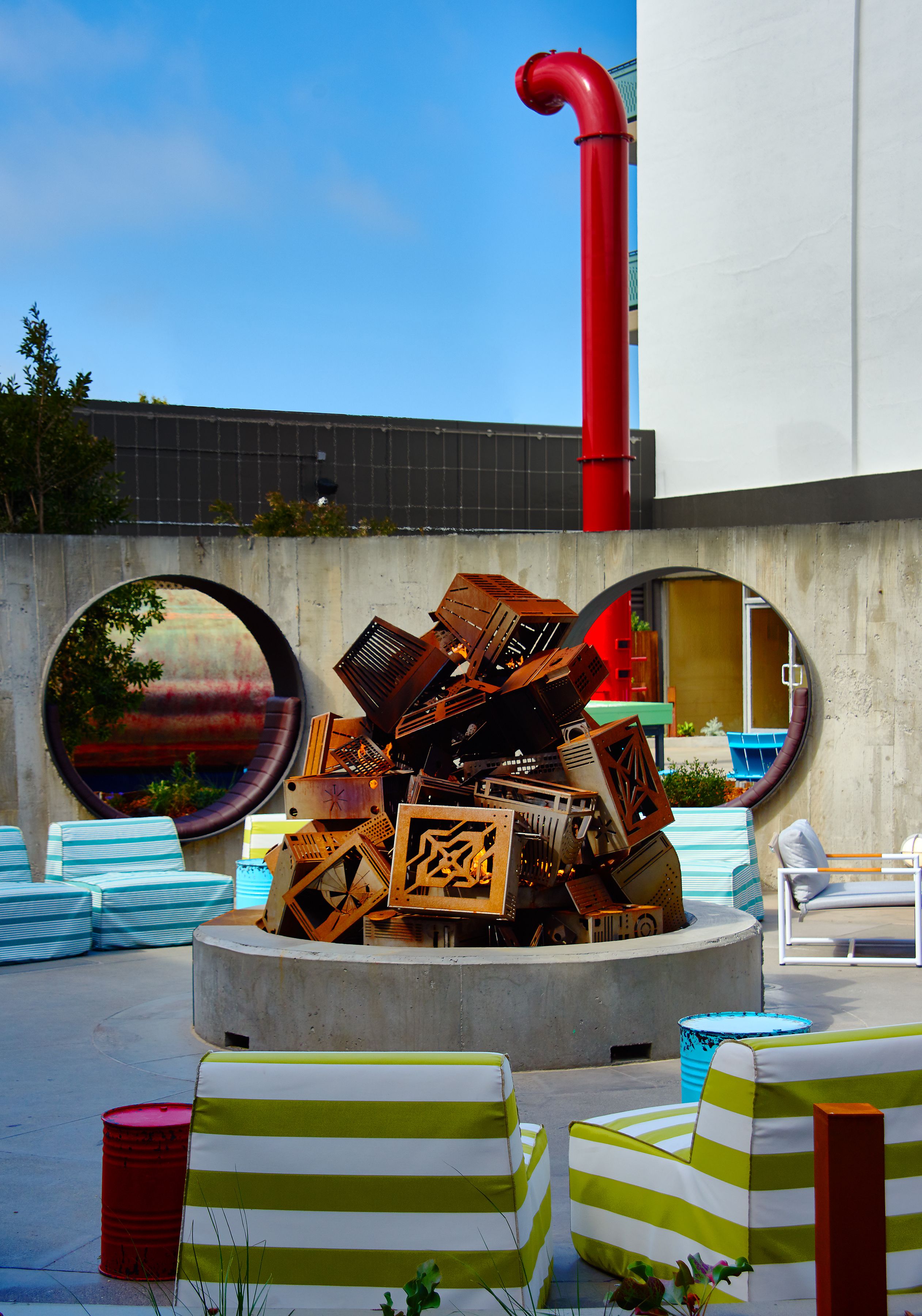 A modern outdoor seating area with circular mirrors, a concrete structure, and striped lounge chairs.