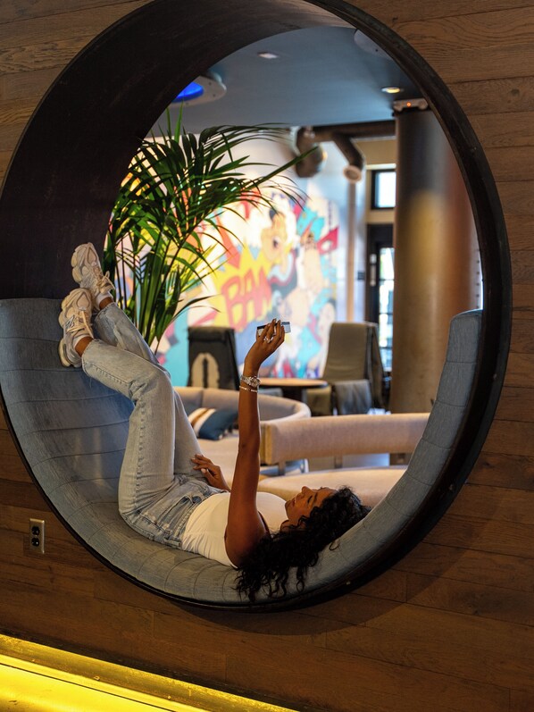 Une personne est allongée dans un espace de détente circulaire, avec une plante et une fresque colorée en arrière-plan.
