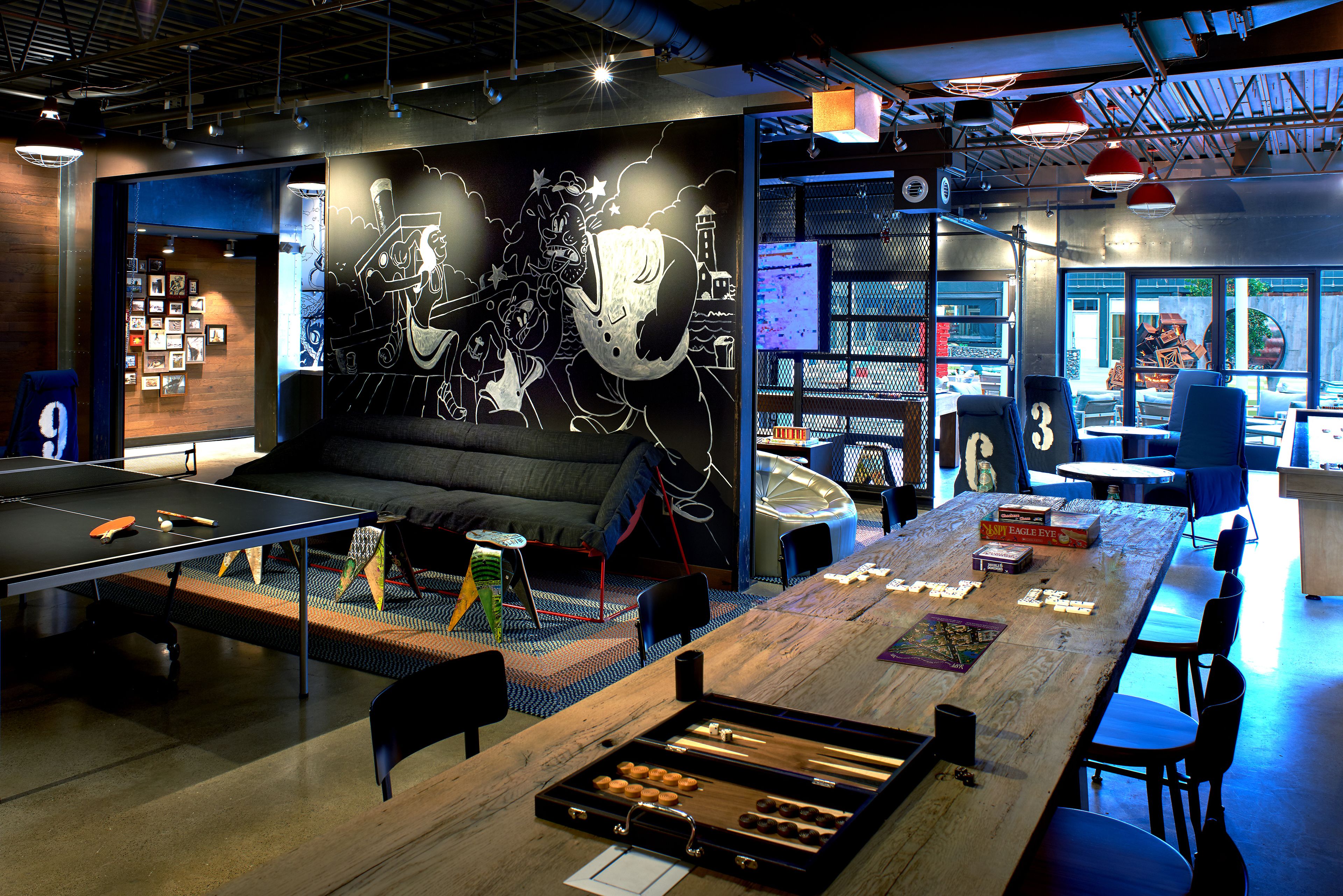 A modern indoor space with a ping pong table, seating area, and a large table with board games.