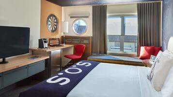 Habitación de hotel con cama, escritorio, televisión, dardos y ventana con cortinas.