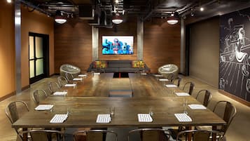 Un salón de conferencias con una larga mesa, sillas y una pantalla grande que muestra una imagen.