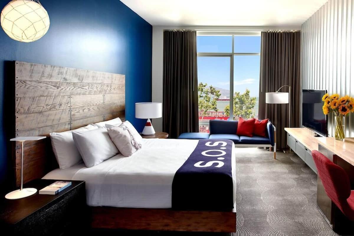 Habitación de hotel con cama, sofá, escritorio y televisor, y vista al exterior.