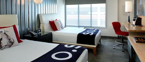 Habitación de hotel con dos camas, un escritorio, una silla, una lámpara y ventana con vista.