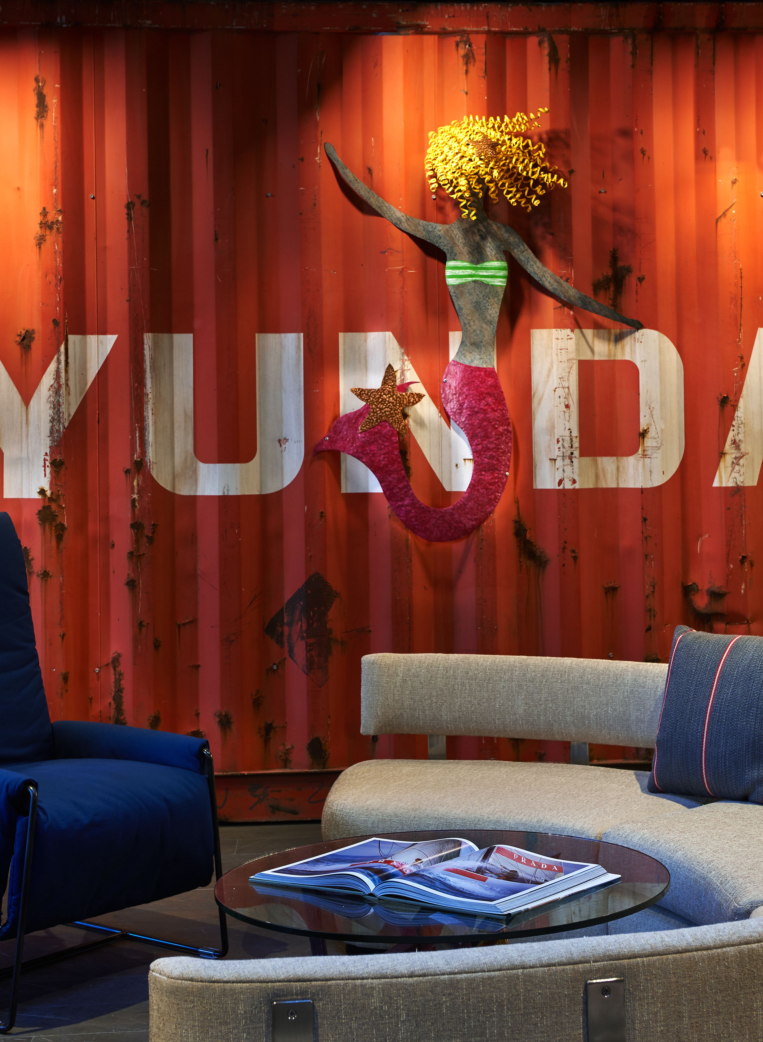 A room with a red wall, a sofa, a chair, and a table with magazines.