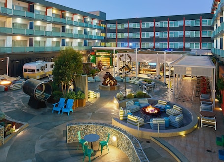 A hotel courtyard with outdoor seating, a fire pit, and a vintage camper parked nearby.