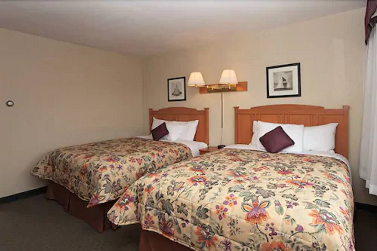 A hotel room with two single beds, each with a floral bedspread and a wooden headboard. There are two wall-mounted lamps and two framed pictures above the beds.