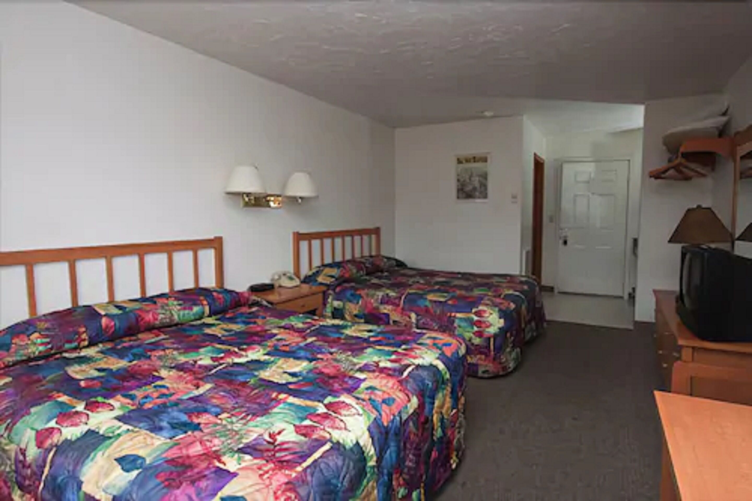 A room with two beds, a desk, a television, and a door leading to another room.