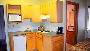 Cocina compacta con armarios de madera, microondas, lavamanos y un refrigerador pequeño.
