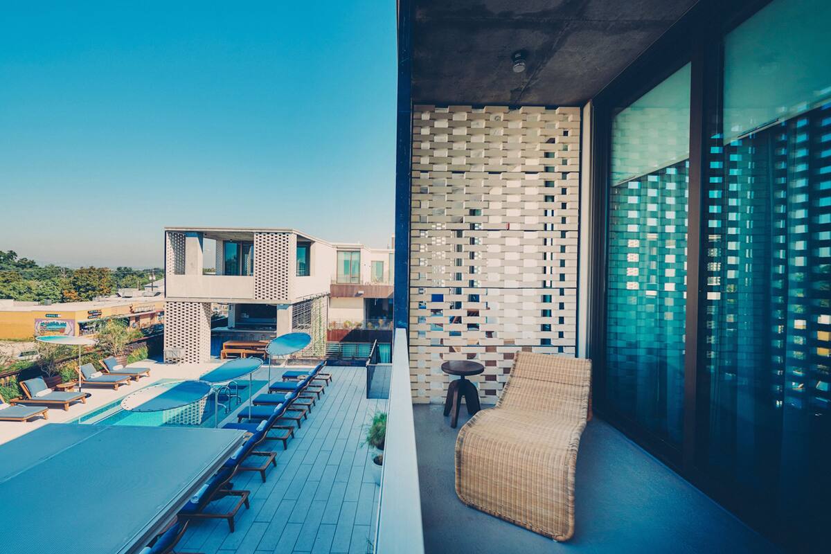 Terraço no telhado com piscina, espreguiçadeiras e um sofá de vime.