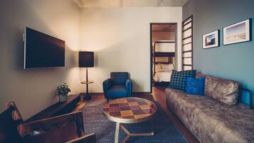 A compact living space with a flat-screen TV, a round coffee table, a sofa, a chair, and a bunk bed.