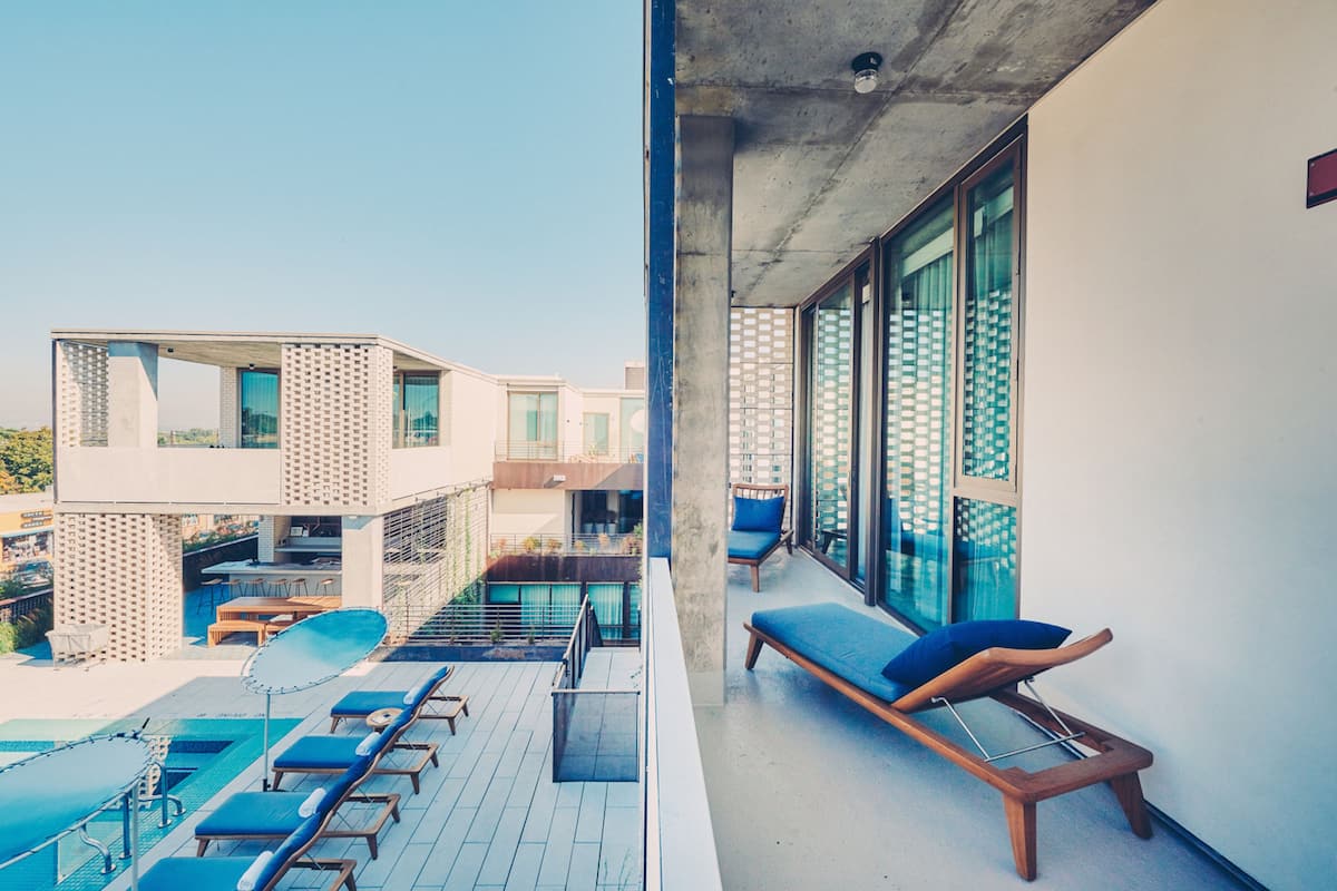 Terraço no telhado com espreguiçadeiras, piscina e um edifício moderno com grandes janelas.