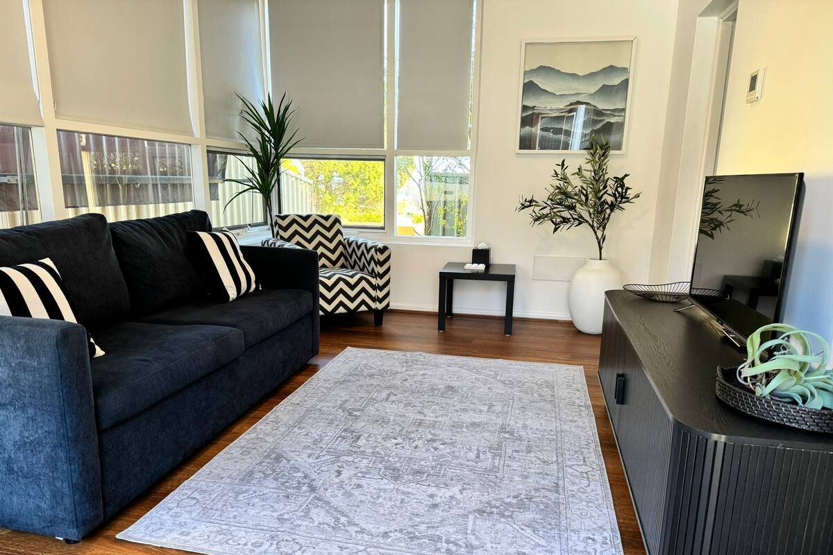 A modern living room with a dark sofa, a patterned rug, a small table, and a TV stand.