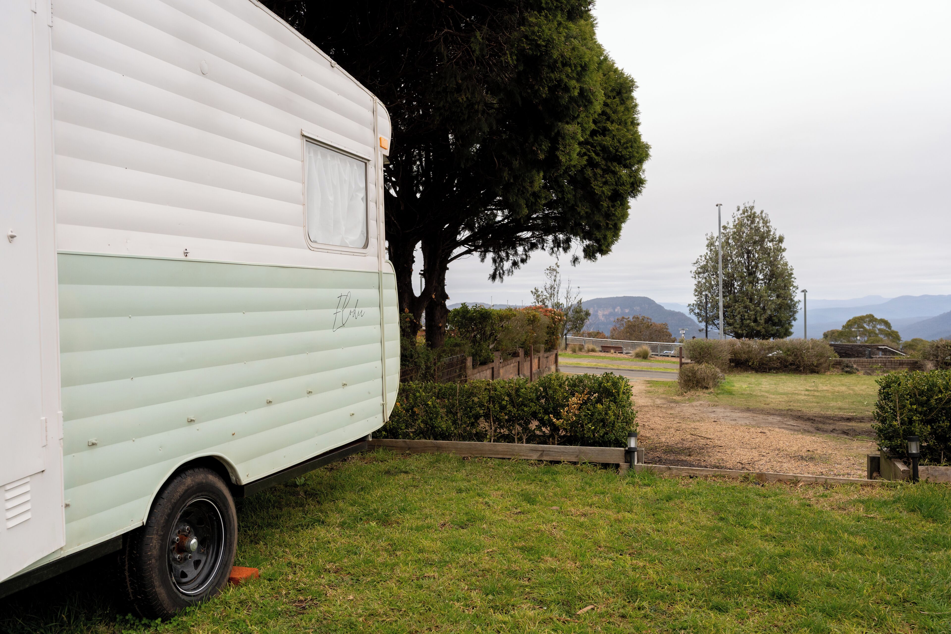 Een witte camper staat op een gazon, met een boom en een hek op de achtergrond.