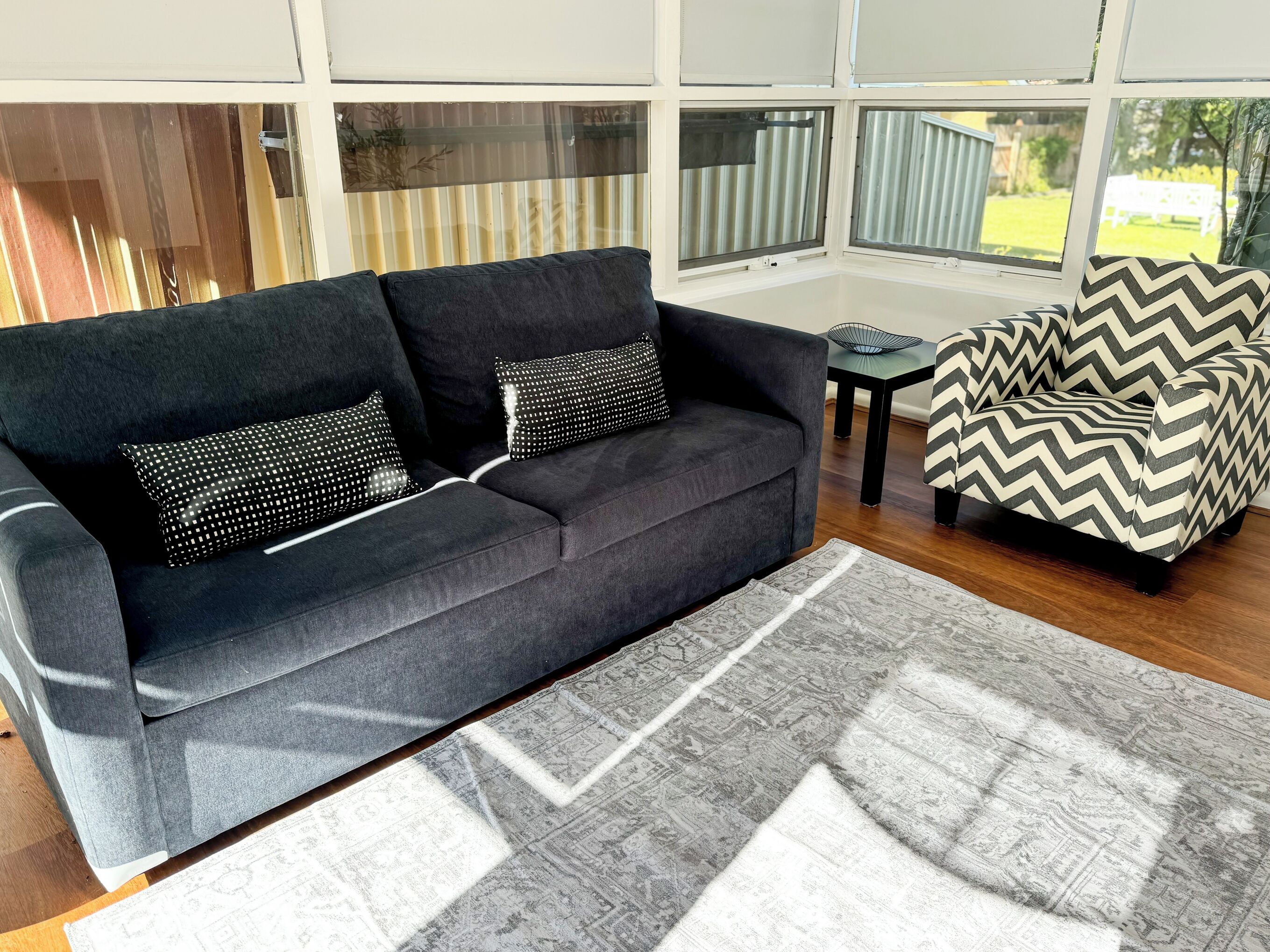 A modern living room with a dark grey sofa, patterned cushions, a patterned rug, and a chevron-patterned chair.