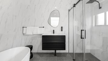 Un baño moderno con bañera, tocador con espejo y ducha con mampara de vidrio.