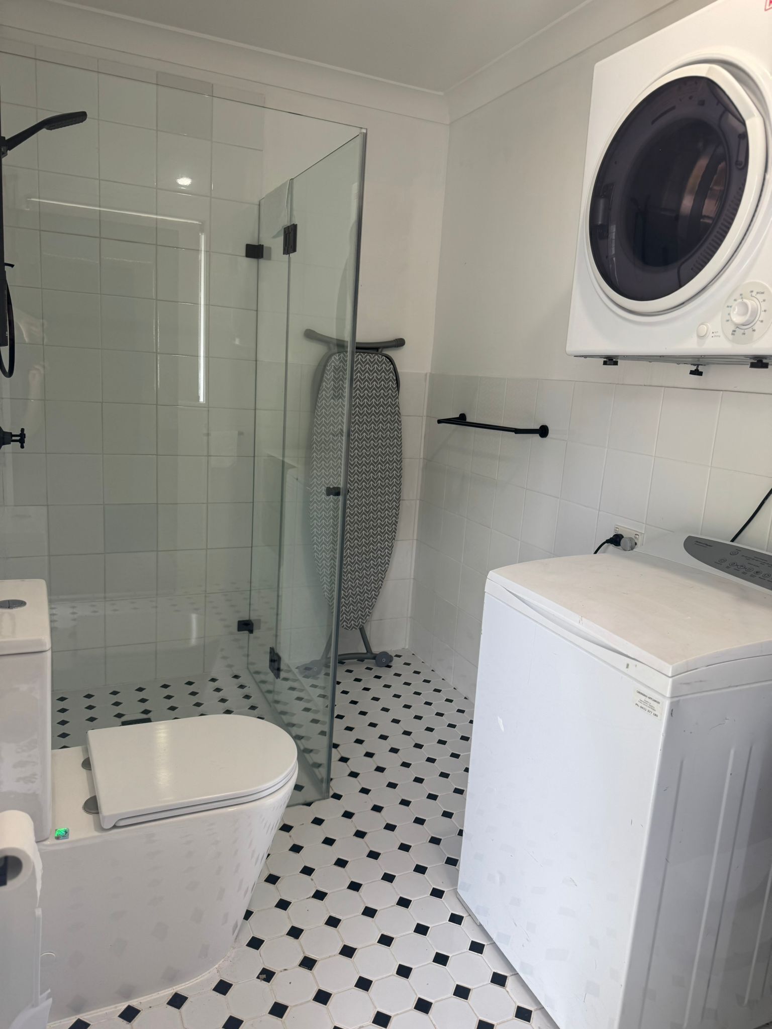 A bathroom with a shower, toilet, and washing machine.