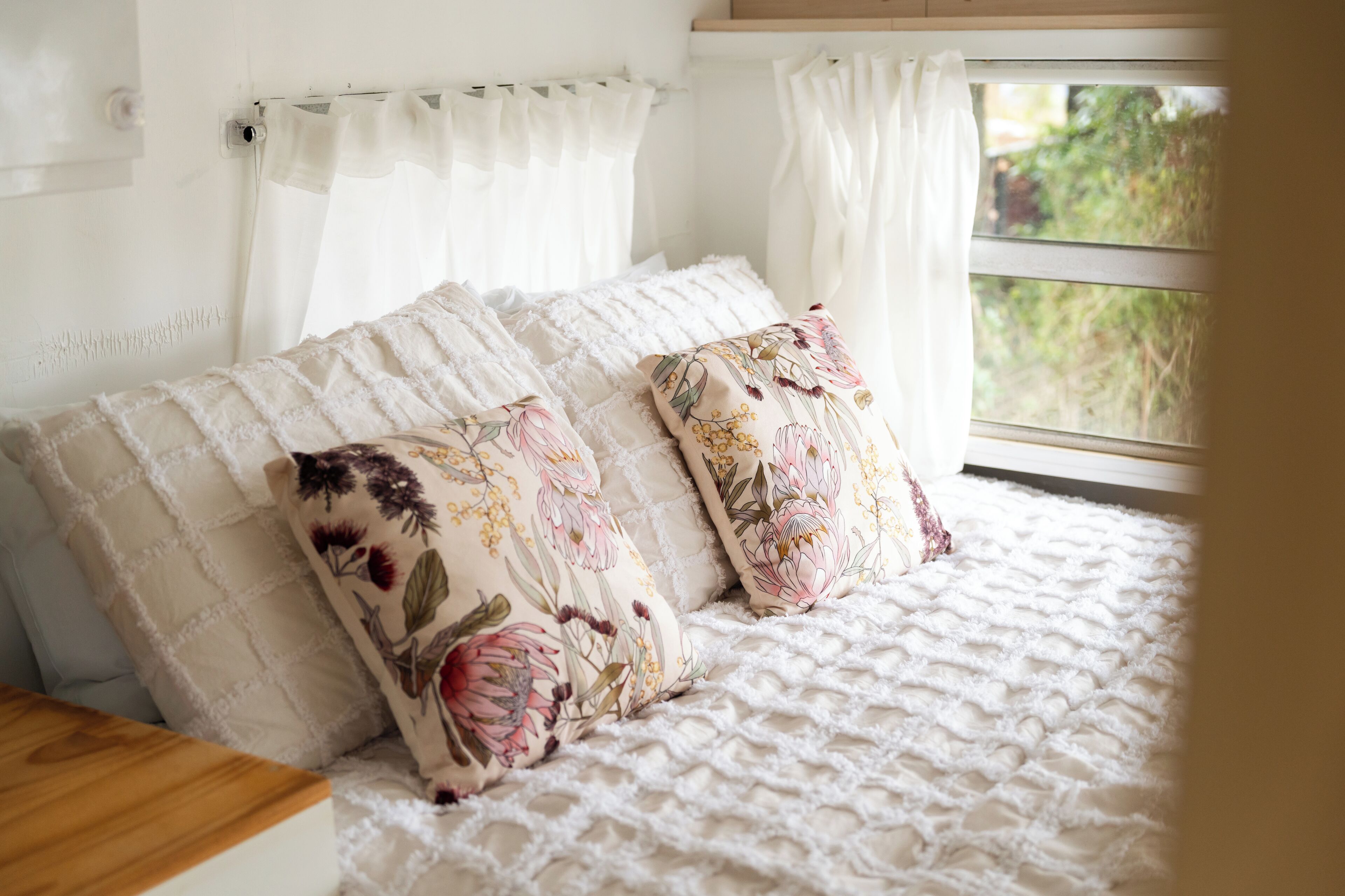 Un lit avec des oreillers à motifs floraux et une couvre-lit blanche à texture particulière.
