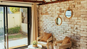 A room with a brick wall, wooden ceiling beams, a large window, and two chairs with cushions. - Montblu at Echo Point (Katoomba)