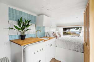 A compact, modern kitchenette with a white fridge, wooden countertop, and a sink.