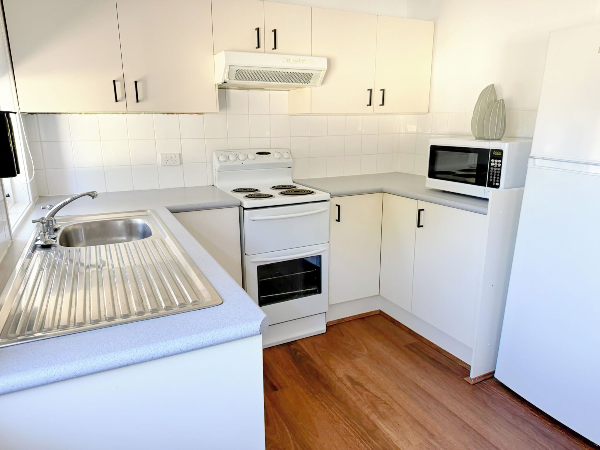 Una cocina moderna con armarios blancos, un lavaplatos de acero inoxidable, una estufa, un horno y un microondas.