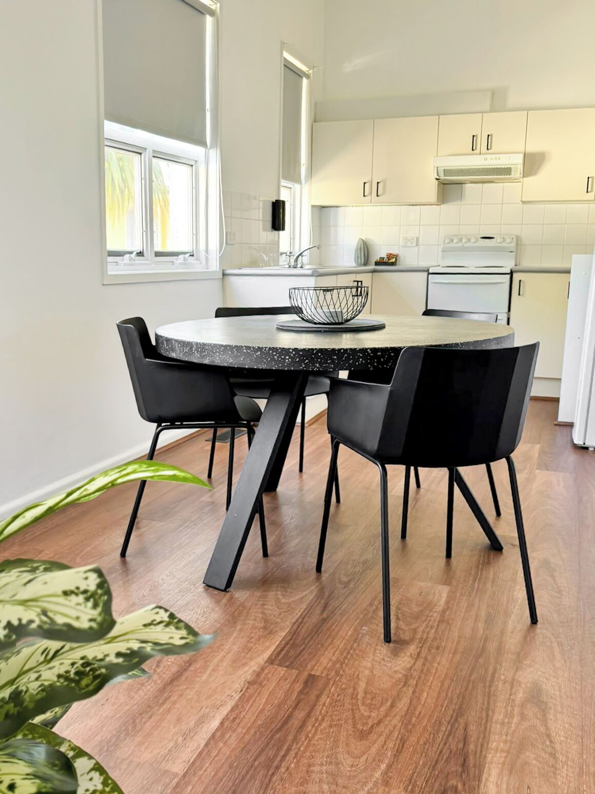 A modern kitchen with a round dining table, black chairs, and a wooden floor.