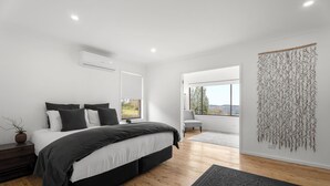 A modern bedroom with a large bed, a bedside table, a wall-mounted air conditioner, and a view of the outdoors. - Montblu at Echo Point (Katoomba)