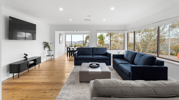 A modern living room with a large TV, dark sofas, a coffee table, and a wooden floor. - Montblu at Echo Point (Katoomba)