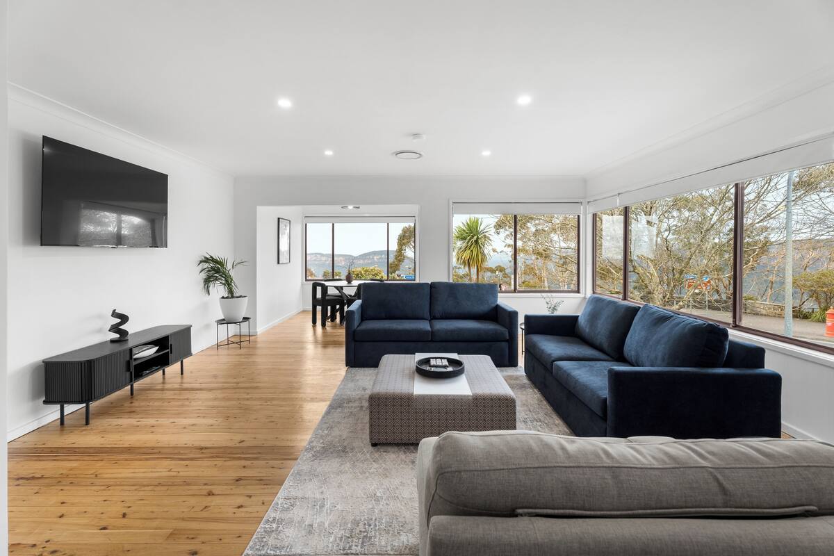 A modern living room with a large TV, dark sofas, a coffee table, and a wooden floor.