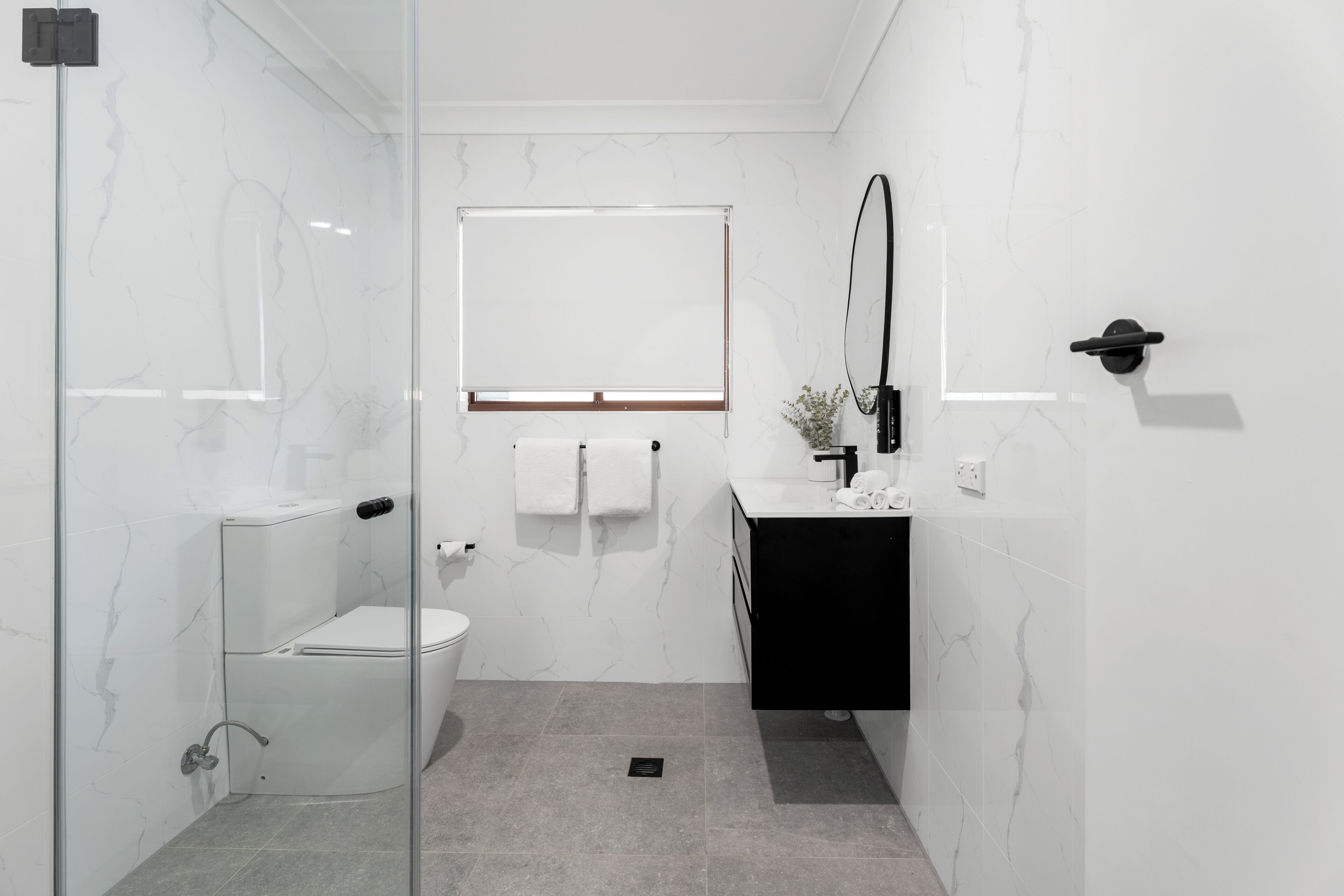 A modern bathroom with a glass shower enclosure, a white toilet, a black sink, and a mirror.