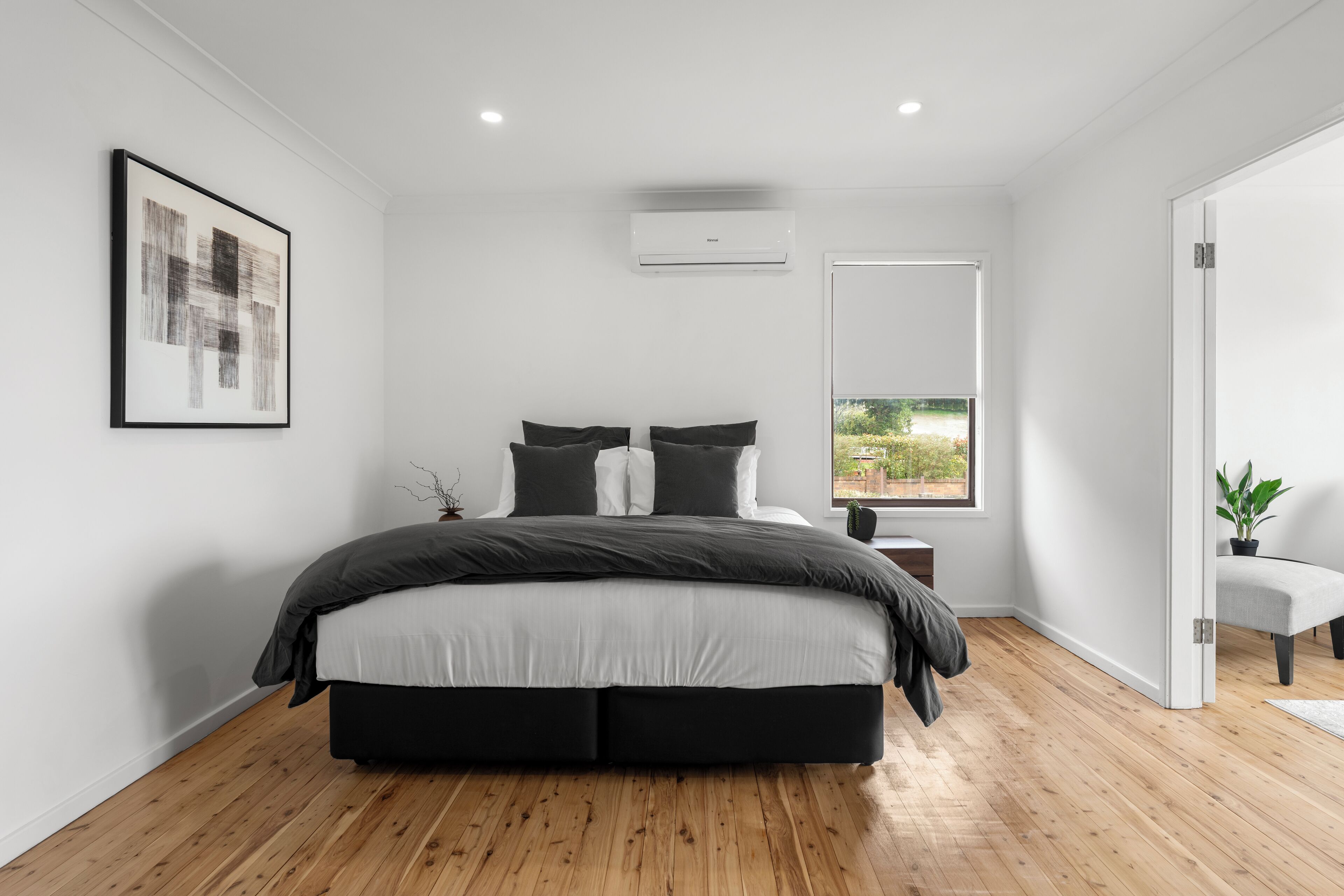 A modern bedroom with a large bed, a window with a view, and a framed artwork on the wall.