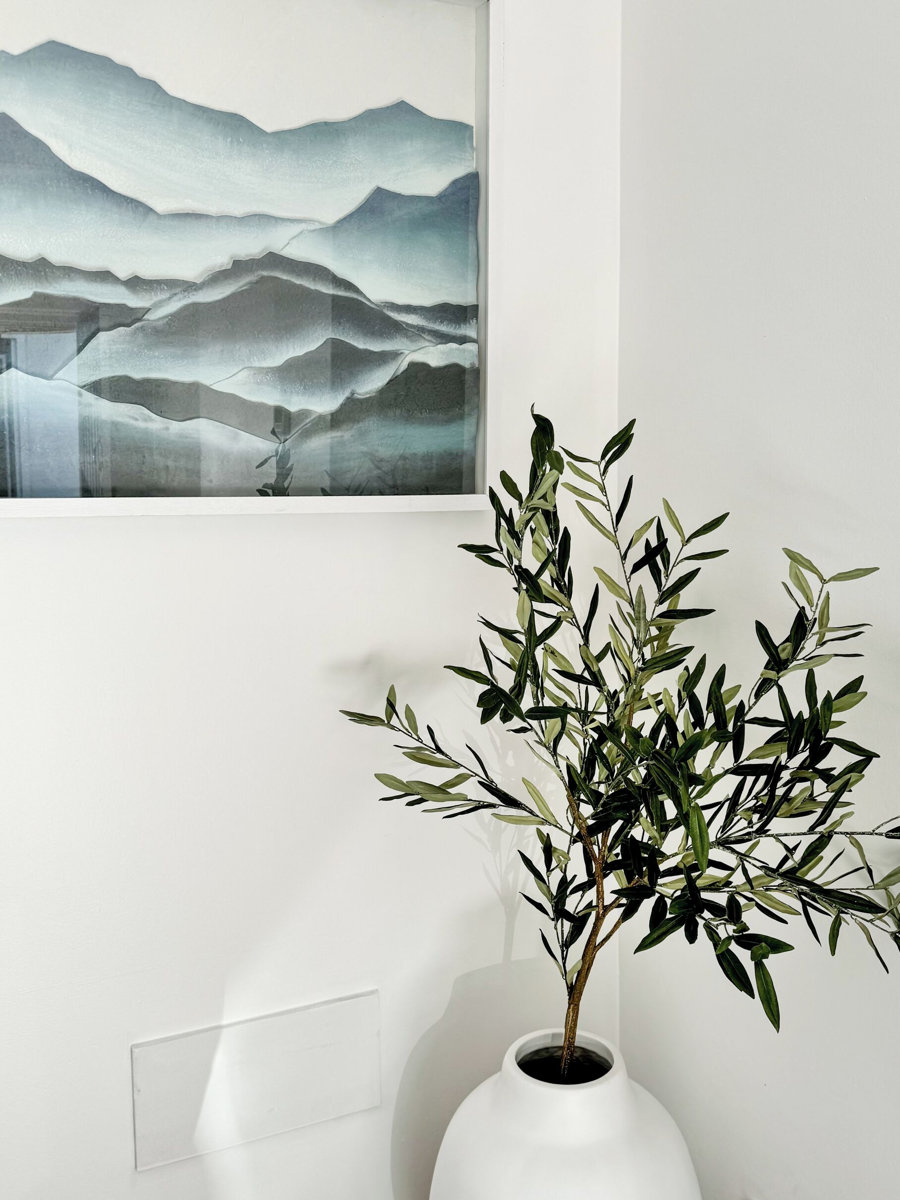 Un vase blanc avec une plante, posé sur un mur blanc.