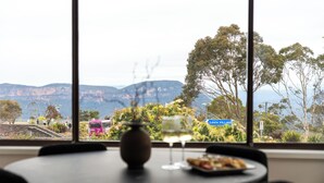 A table with a vase, two wine glasses, and a plate of food. A window reveals a view of a train, trees, and a sign reading "Leva Village". - Montblu at Echo Point (Katoomba)