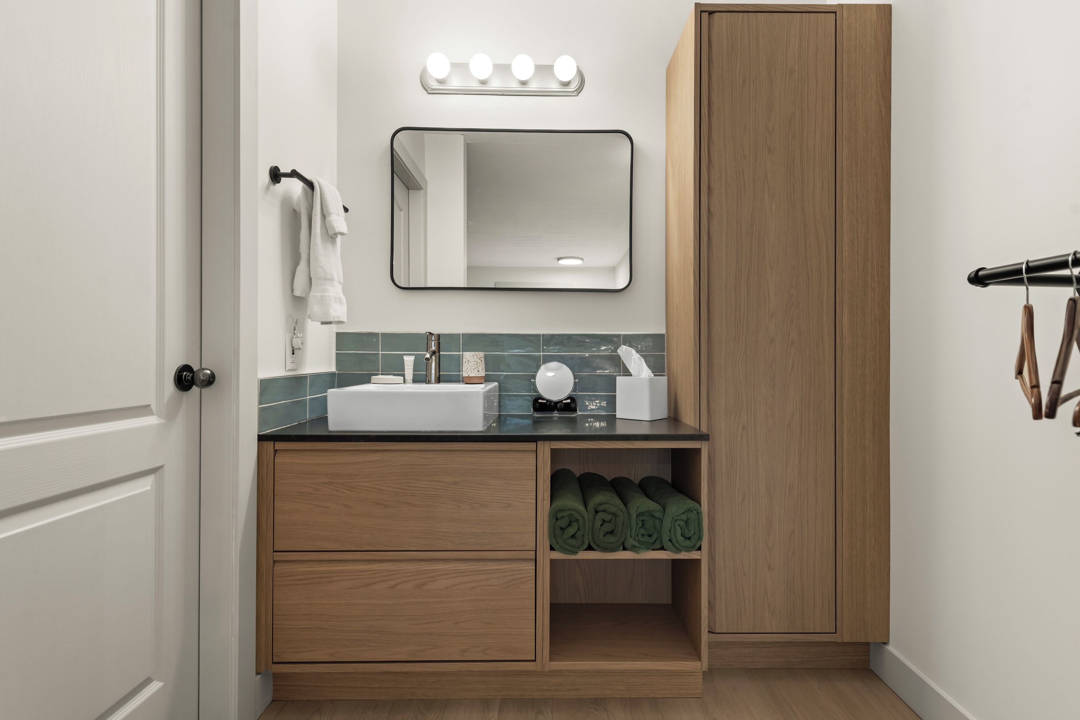A bathroom with a sink, mirror, vanity, towel rack, and wooden cabinet.