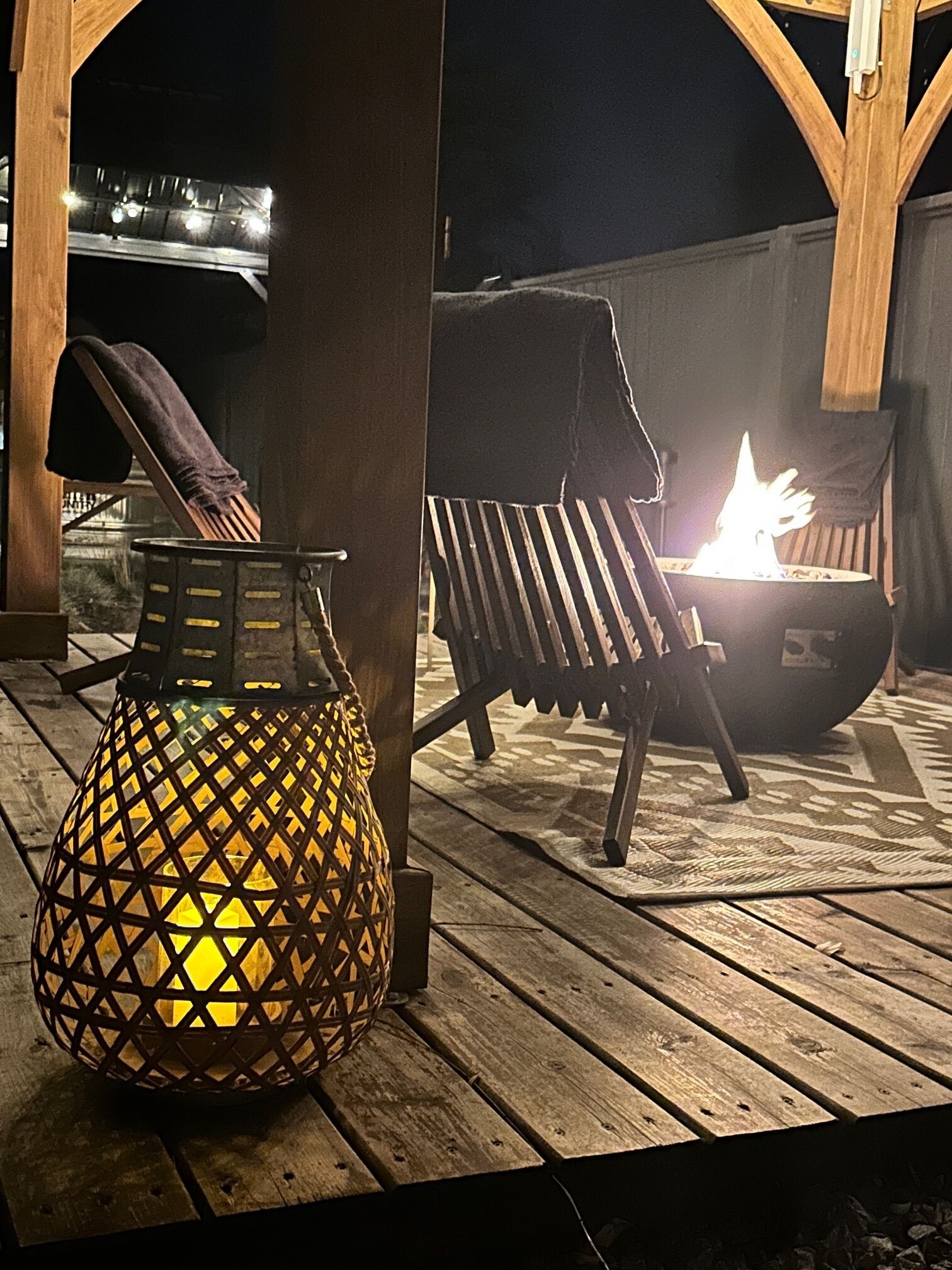Une terrasse en bois avec une lanterne en métal, un foyer et un fauteuil de relaxation.