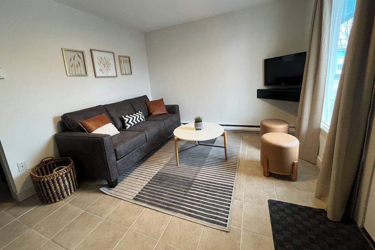 A modern living room with a sofa, a coffee table, a TV, and a window with curtains.