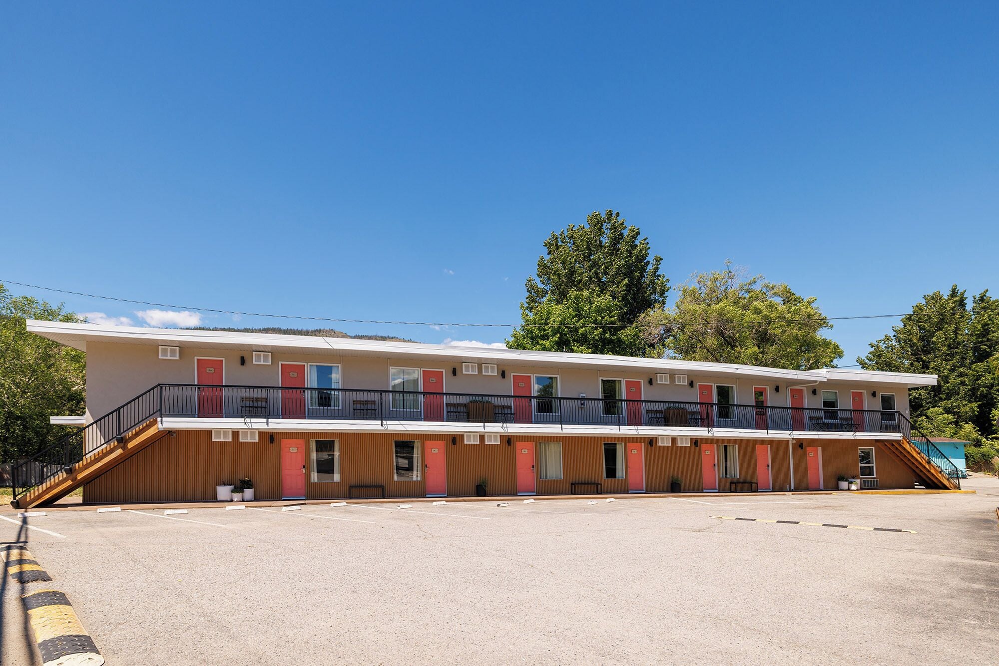 A motel with a two-story structure, a parking lot, and a clear blue sky.