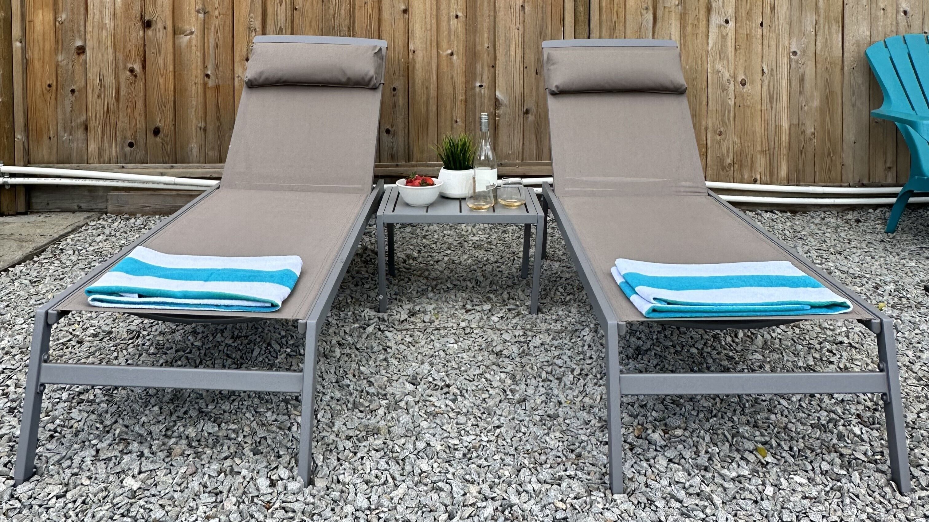 Two lounge chairs with towels, a small table with a plant, a bottle, and a bowl of strawberries.