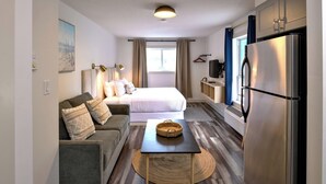 Habitación de hotel compacta con cama, sofá, mesa de comedor y refrigerador.
