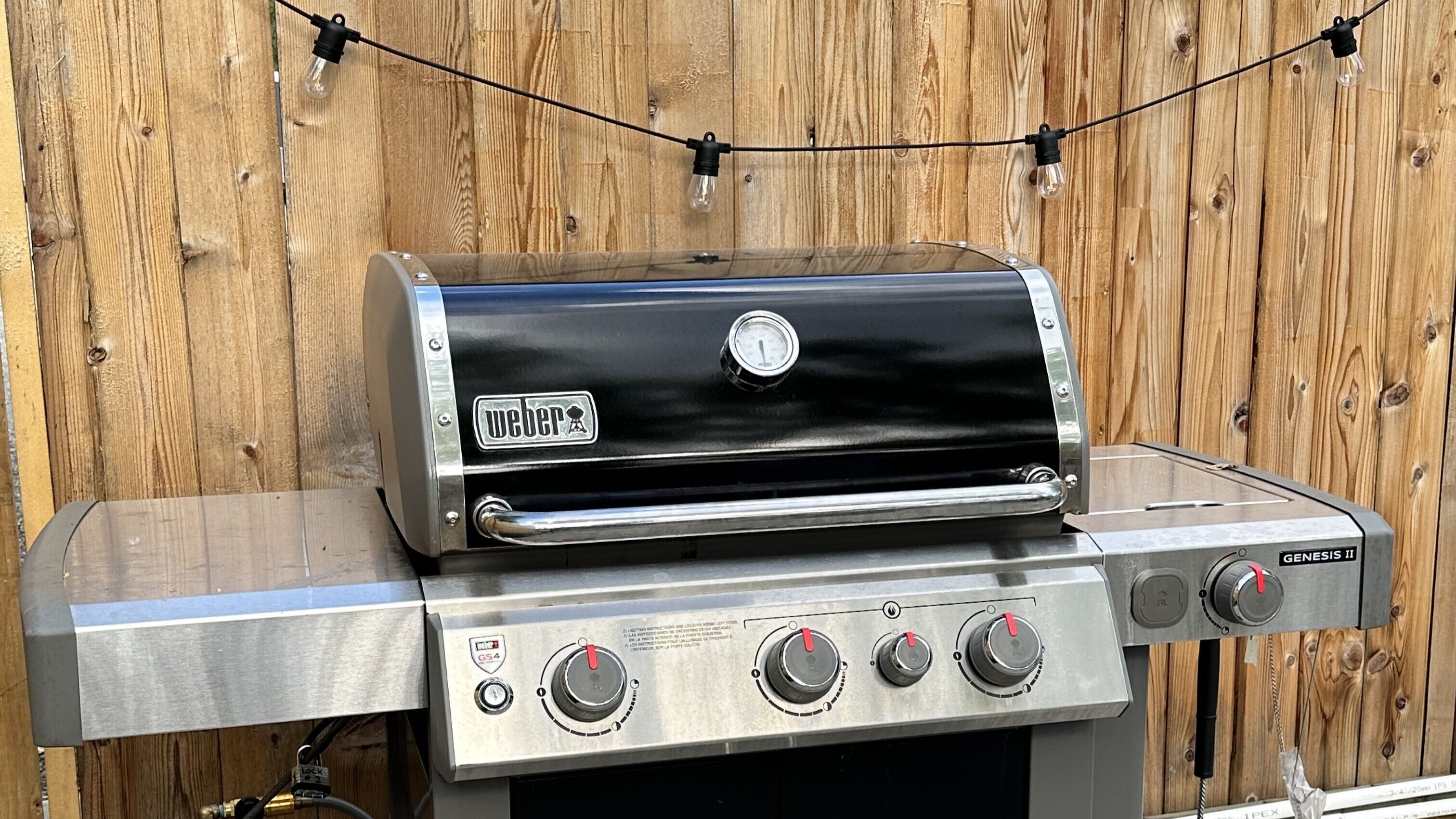 Una parrilla de gas Weber Genesis II con acabado de acero inoxidable, un termómetro digital y cuatro perillas de control.