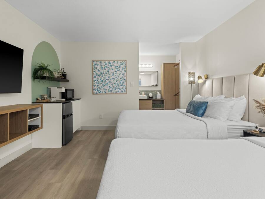 Une chambre d’hôtel moderne dotée d’une télévision à écran plat, d’un bureau avec un ordinateur, d’un lit avec une literie blanche et d’une grande fenêtre.
