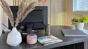 Un mostrador de recepción de diseño moderno, con un televisor de pantalla plana, una planta en maceta y un jarrón decorativo con plumas de pampa.