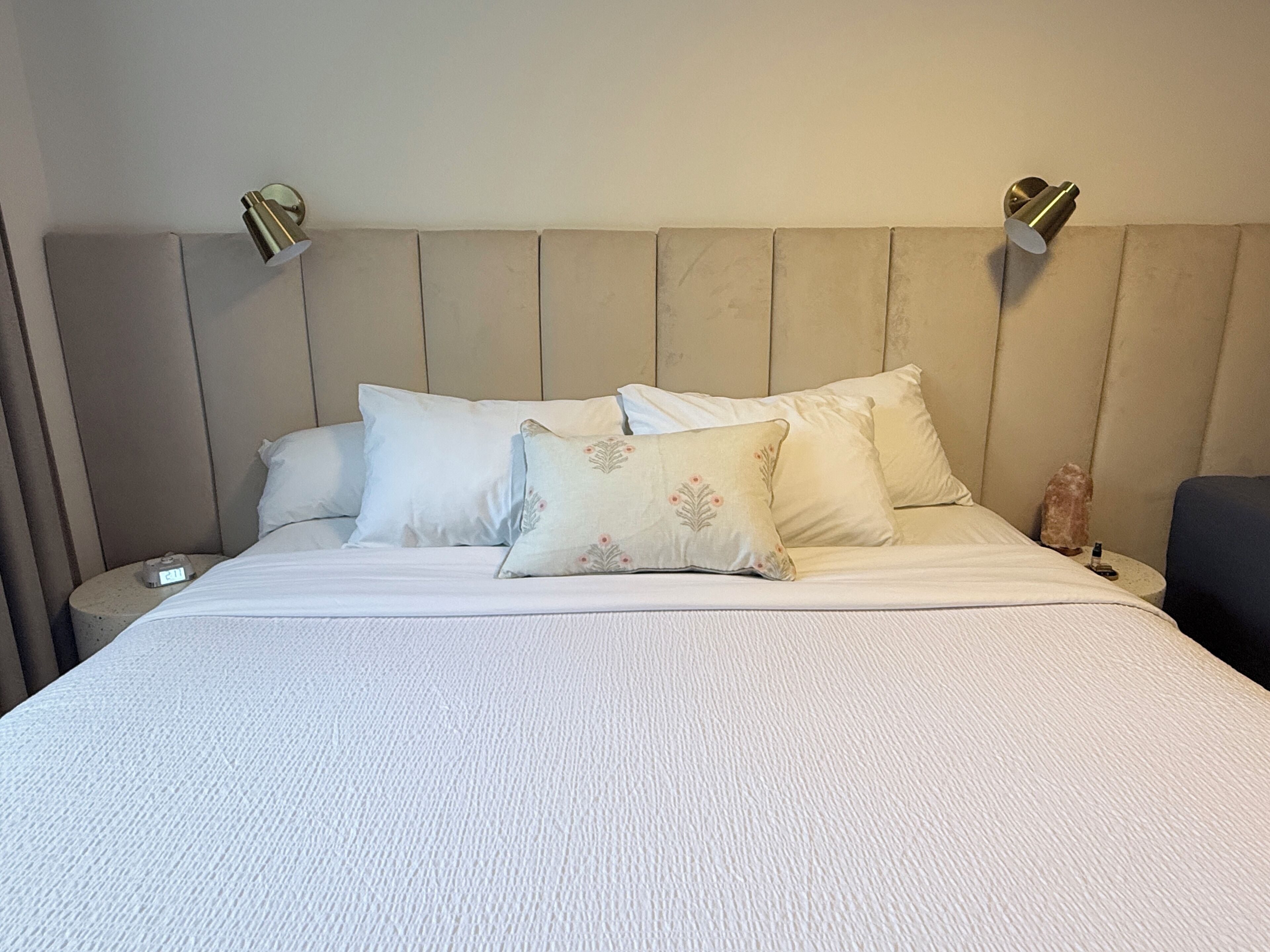 Una cama con una colcha blanca texturizada, dos mesitas de noche y dos lámparas de pared.