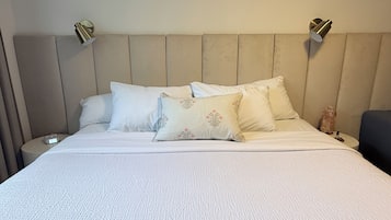 Una cama con una colcha blanca texturizada, dos mesitas de noche y dos lámparas de pared.