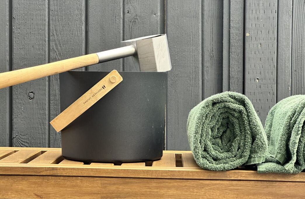 A black pot with a wooden handle and a metal blade, a rolled green towel, and a wooden rack.