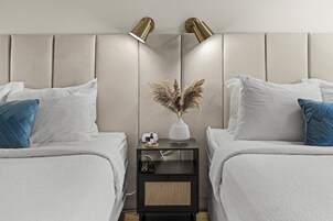 Habitación de hotel con dos camas, una mesita de noche con lámpara, un jarrón con plantas secas y una pequeña mesa con cámara y control remoto.